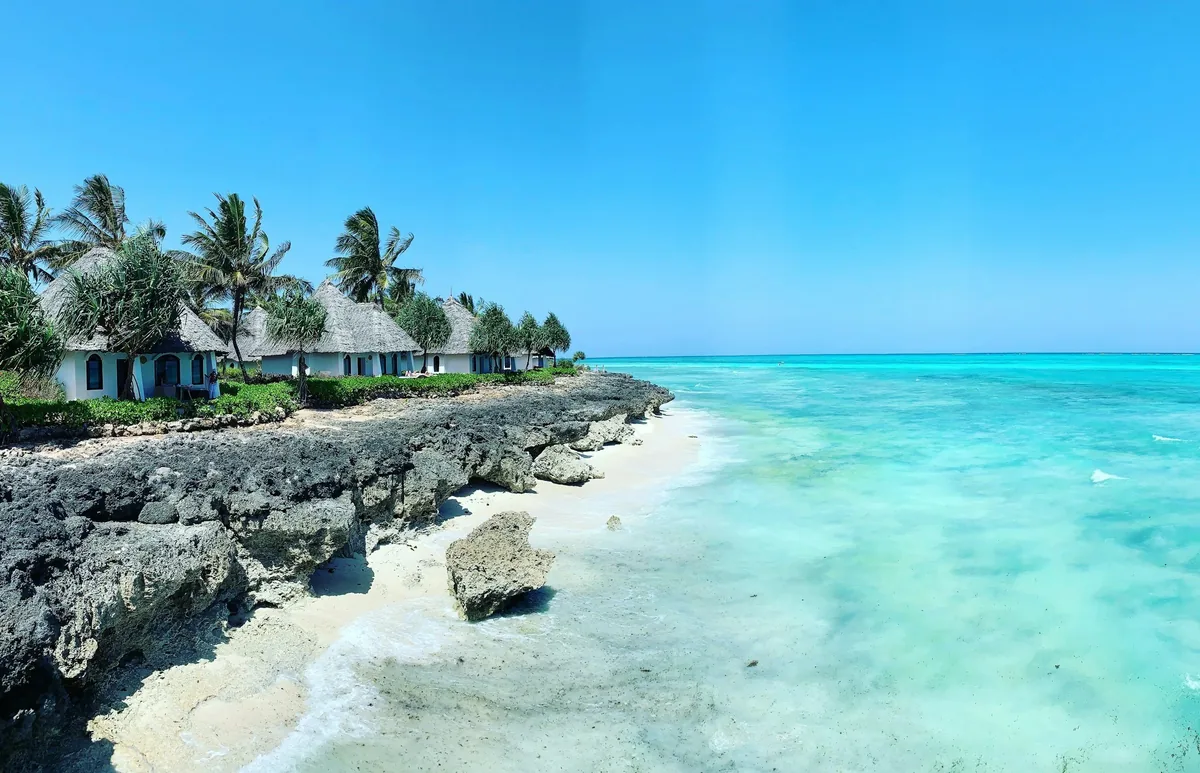Türkisfarbenes Meer mit Strandbungalows und Palmen auf Sansibar